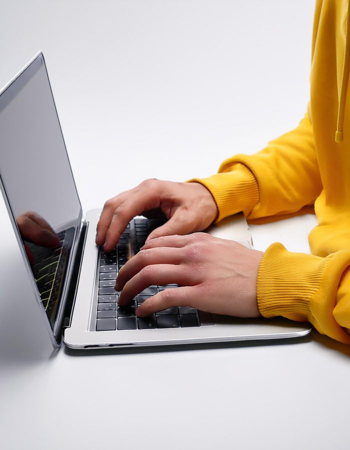 Firefly Manos en una laptop, se ven las mangas de un buzo amarillo y el fondo es blanco. El angulo d